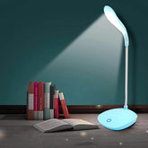 Blue LED desk lamp illuminating an open book on a wooden surface with a teal wall background.