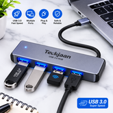 Teckjaan USB 3.0 hub with multiple USB ports, shown connected to a laptop on a marble desk with various USB drives plugged in.
