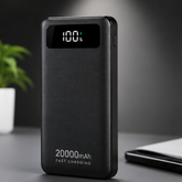 A black portable power bank with a textured finish, featuring a digital display showing 100% battery level and '20000mAh FAST CHARGING' printed on the front, set on a dark gray surface.