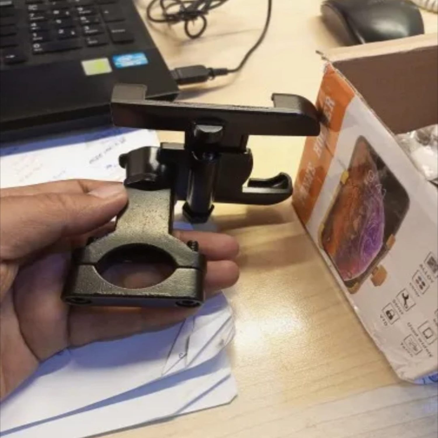 Hand holding a metal clamp on a desk with a laptop and box in the background