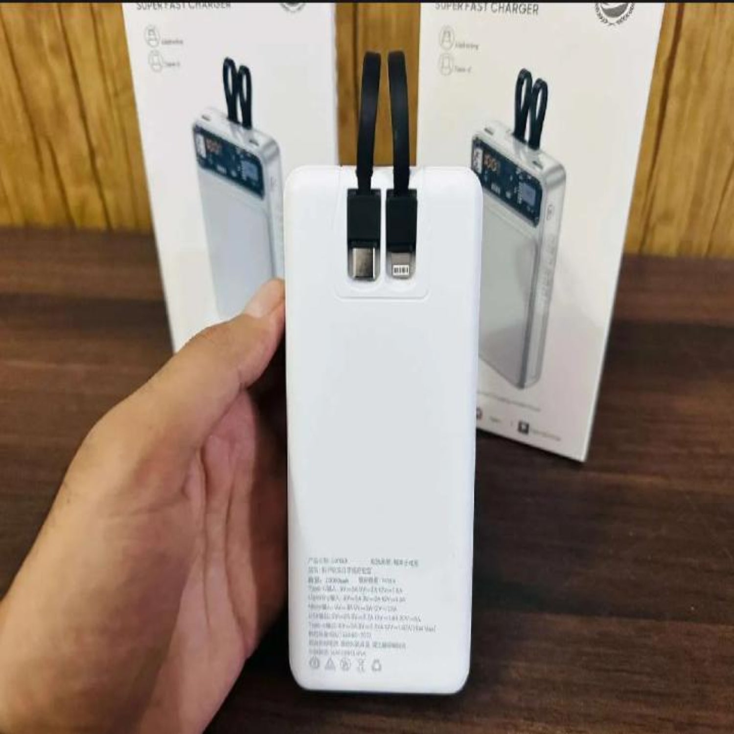White power bank with USB cable on a wooden surface with packaging in the background.