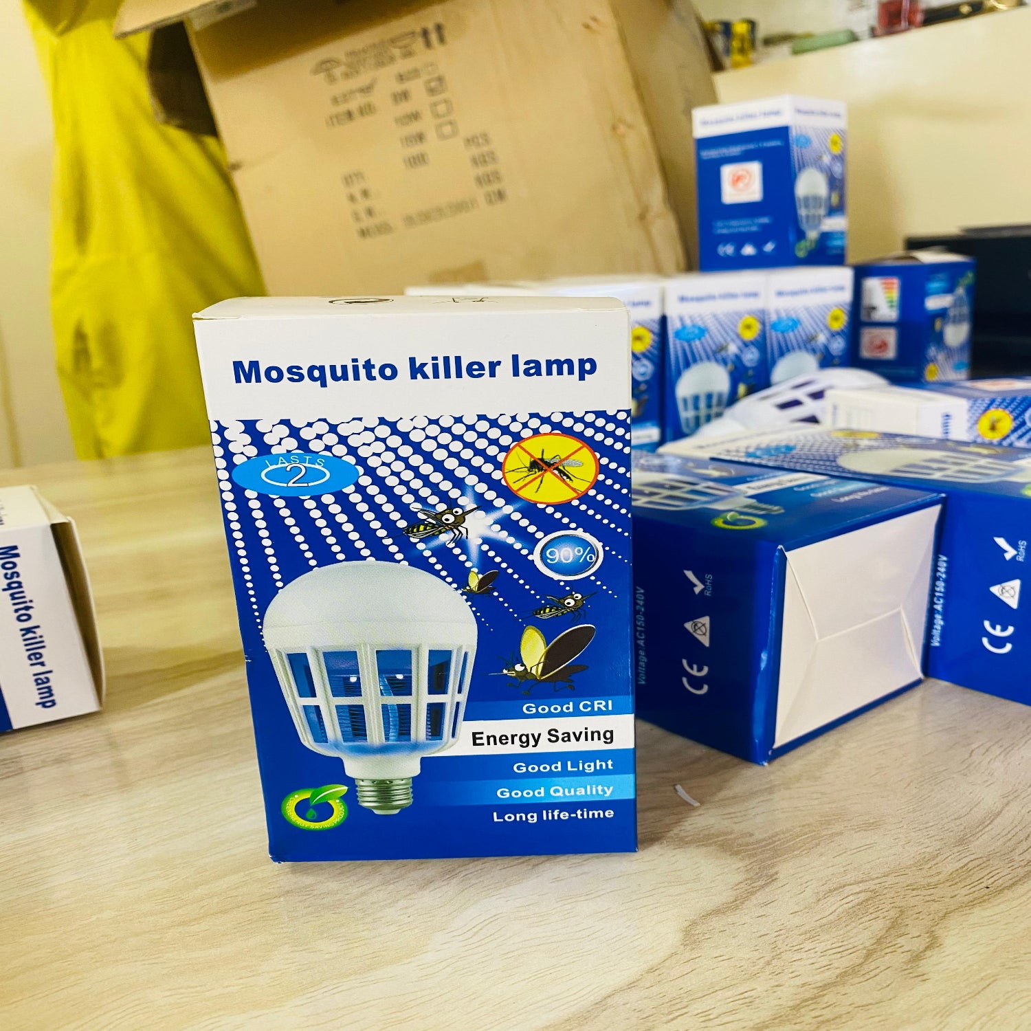 Mosquito killer lamp packaging on a wooden surface with other products in the background.