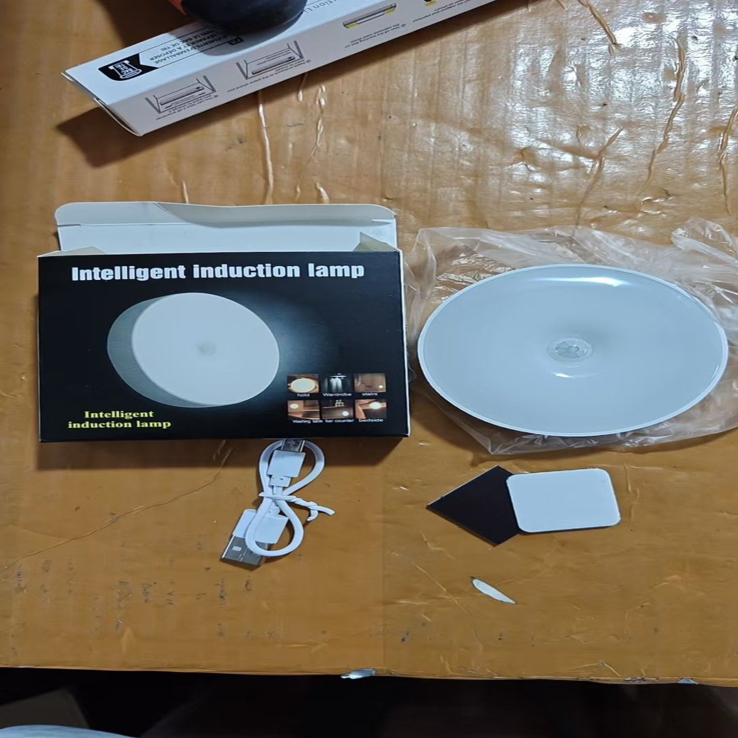 Intelligent induction lamp with packaging, base, and sensor on a wooden surface