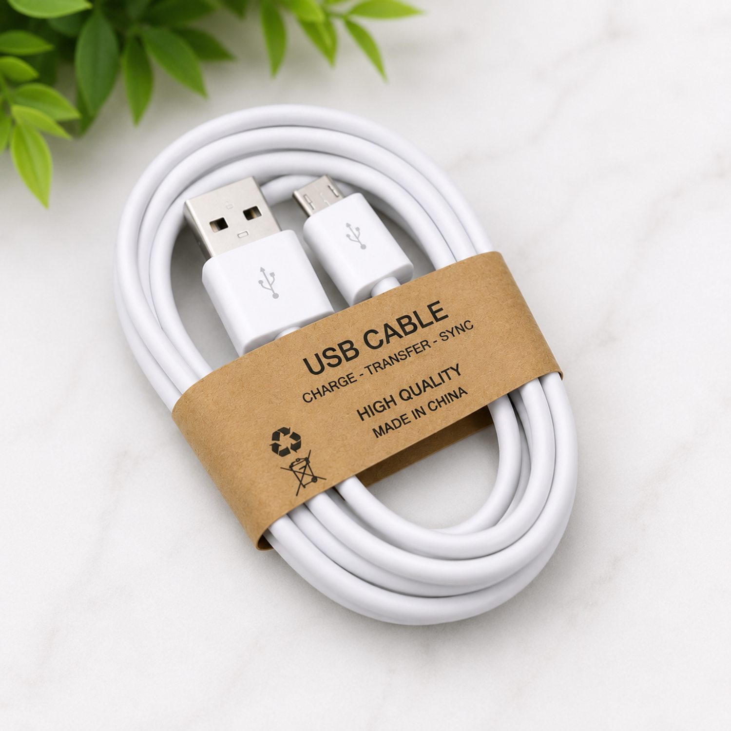 A white USB cable coiled and wrapped with a brown kraft paper band labeled 'USB CABLE CHARGE - TRANSFER - SYNC HIGH QUALITY MADE IN CHINA', photographed on a light marble surface with green leaves in the corner.