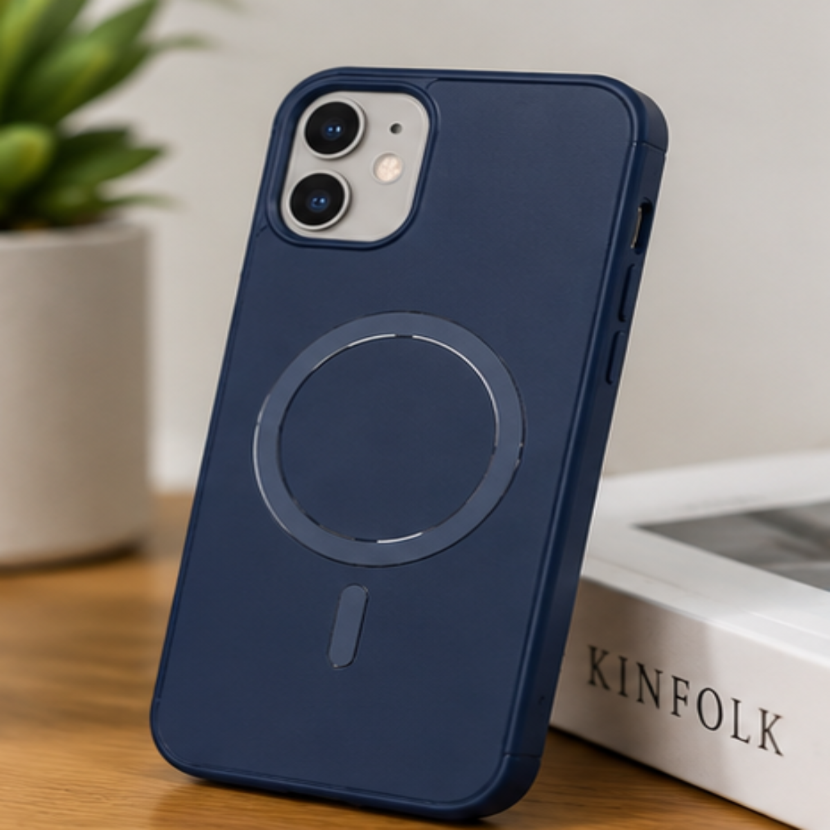 A dark navy blue protective phone case with a circular MagSafe ring, shown on an iPhone standing on a wooden surface next to a book.