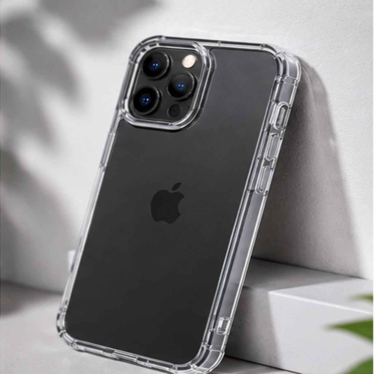 A clear, transparent protective phone case shown on a black iPhone, photographed in a clean, modern setting against a light gray wall and white block.