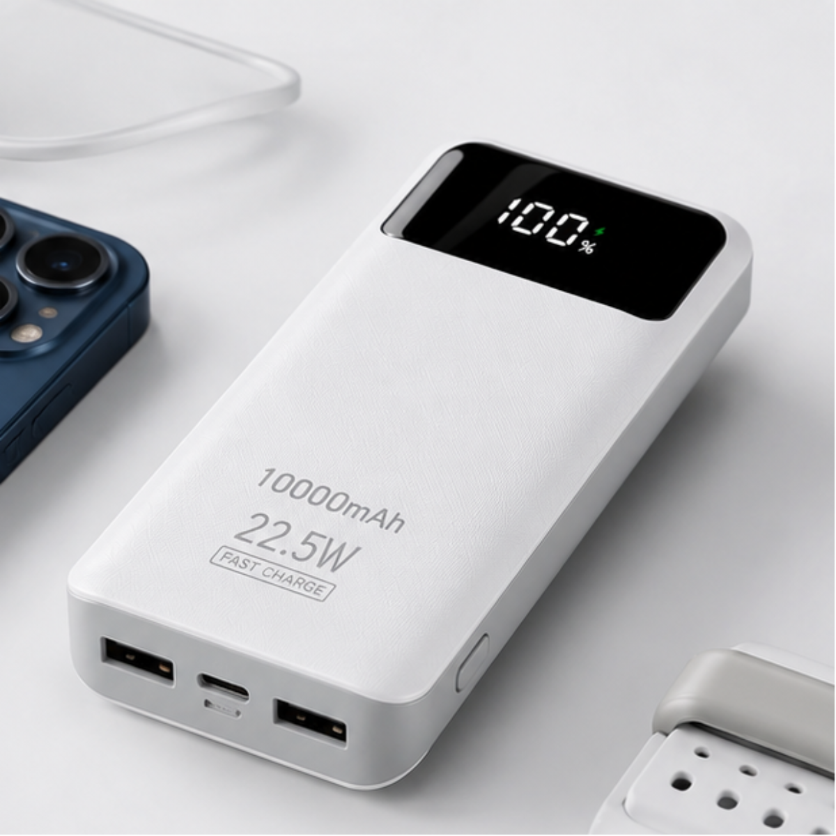 A white 10000mAh portable power bank with a black digital display showing 100% battery, featuring 22.5W fast-charging ports, shown on a clean light gray surface next to a blue smartphone.